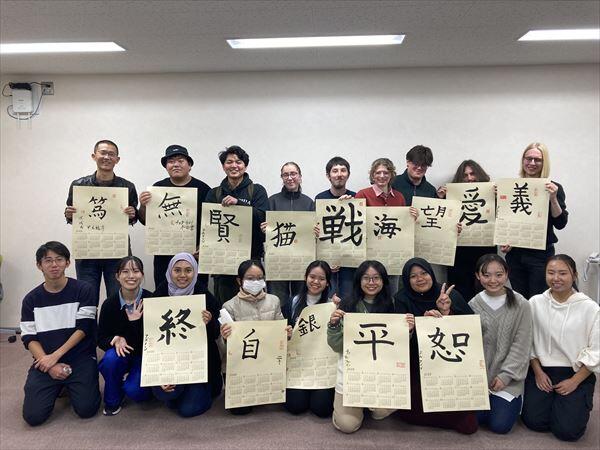 来年のカレンダーに詩文の好きな漢字を書いた作品を持って集合写真