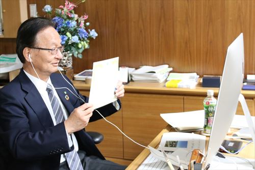 画面越しの受賞者に賞状を見せる駒田学長